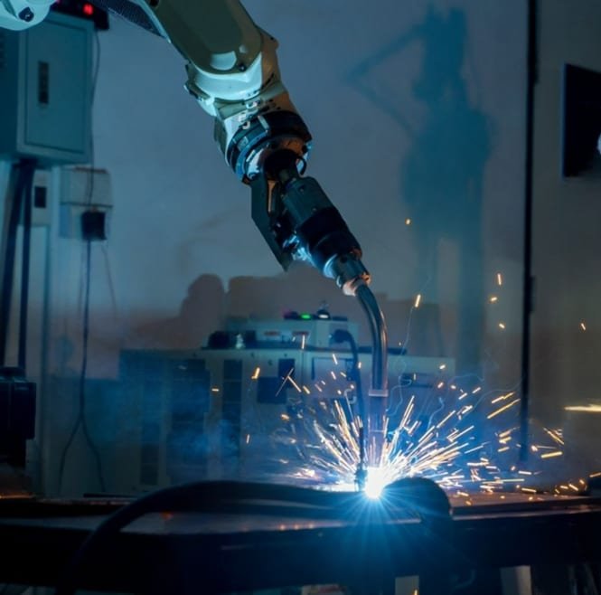Robotic welding arm performing an automated MIG weld with sparks flying